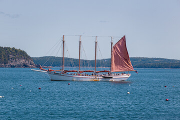 Distinctive red sails being lowered aboard the four-masted wooden schooner Margaret Todd while sailing in Frenchman Bay near Bar Harbor, Maine, with a coastal island nearby. September 8, 2028 © Katie Dobies