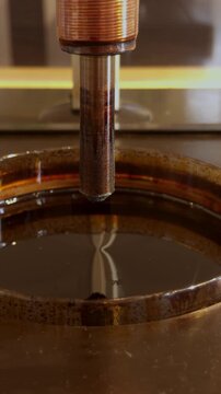 Vertical macro view of ferrofluid rising into sharp spikes around a metal probe under magnetic force.