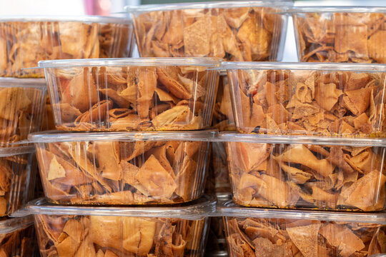 Multiple clear plastic food containers filled with homemade, crusty baked pita bread chips. The bite-sized square snacks are golden brown. The whole-grain pita food is for sale at a farmers' market. 