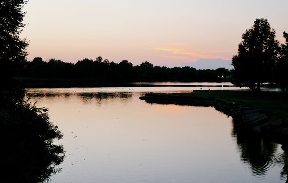 Silhouetted ducks swimming across a peaceful suburban park lake during a vibrant golden hour sunset, reflecting tranquility serene urban wildlife
