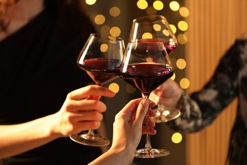 Obraz premium Friends clinking glasses of wine against blurred lights indoors, closeup