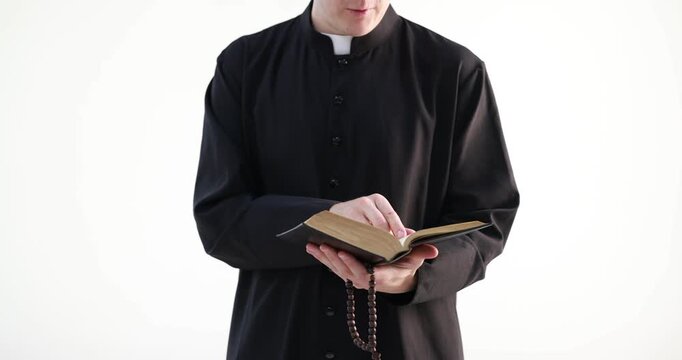 Priest in cassock with rosary reading Holy Bible on white background, closeup