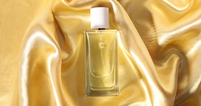 Bottle of aromatic perfume on yellow silk, top view. Camera spinning