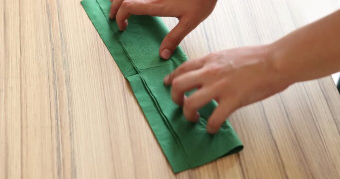 Woman folding green napkin at wooden table, closeup