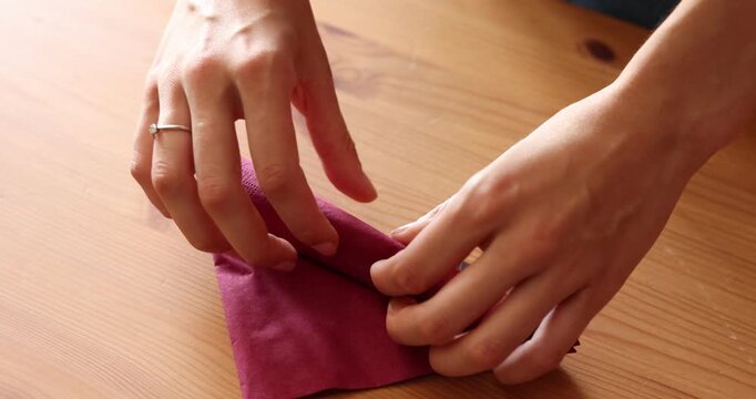 Woman rolling red napkin at wooden table, closeup