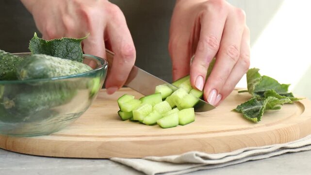 Woman cutting cucumber at grey table, closeup