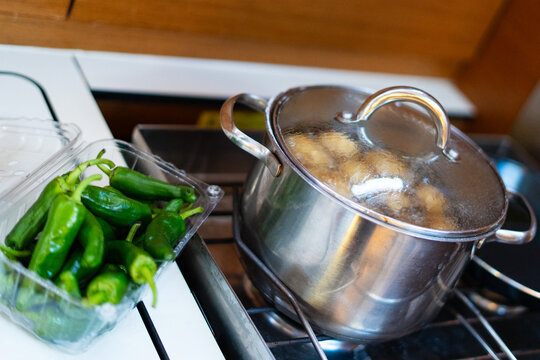 Galley of a sailing yacht with potatoes boiling on the gimballed stove and padron peppers ready on the worktop