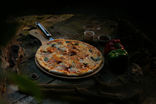 Freshly baked Italian pizza served on a wooden peel with peppers and condiments on a rustic dark wooden table