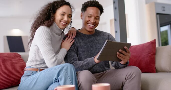 African American couple on sofa, man tapping tablet, woman leaning and pointing, viewing content