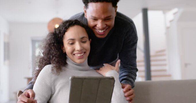 African American couple on sofa, woman tapping tablet in olive case drawing man leaning and hugging