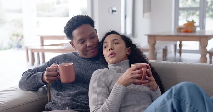 Couple holding twin mugs on couch in sunny home, woman leaning sharing story, man listening smiling