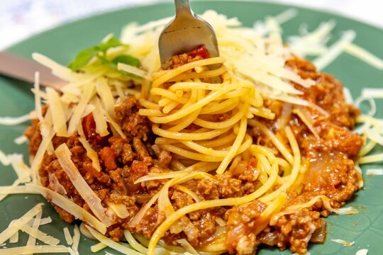 Close-up of homemade spaghetti bolognese served on a green ceramic plate, topped with slow-cooked ground beef in tomato sauce, shavings of grated parmesan cheese 