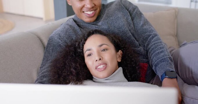 African American couple lounging on living room sofa watching laptop, relaxing together and smiling