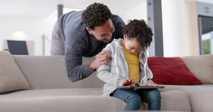 African American father and daughter leaning to see tablet on sofa, father guiding tapping for help