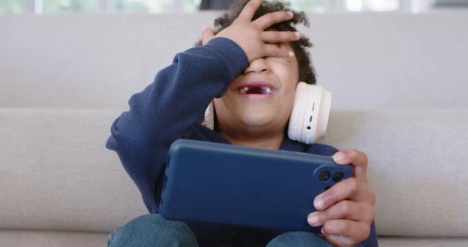 African American child playing on blue smartphone on sofa at home, laughing at clip