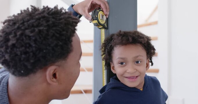 African American father placing tape at post measuring daughter and marking with pencil near stairs