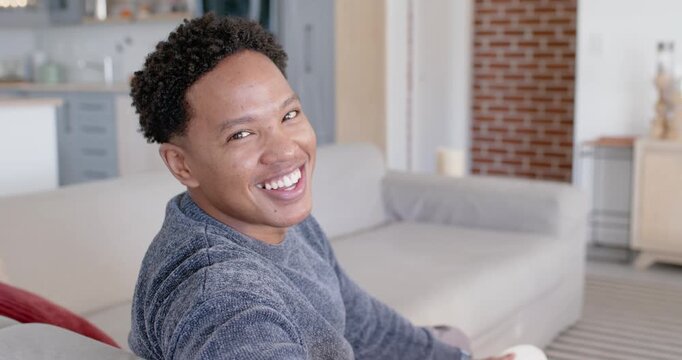 African American man reacting to offscreen cue, laughing and reaching with white disc on sofa