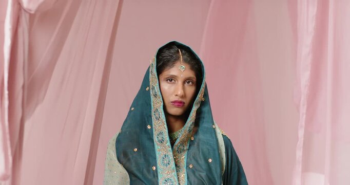 Indian woman standing in set with camera pulling back, lifting teal dupatta revealing maang tikka