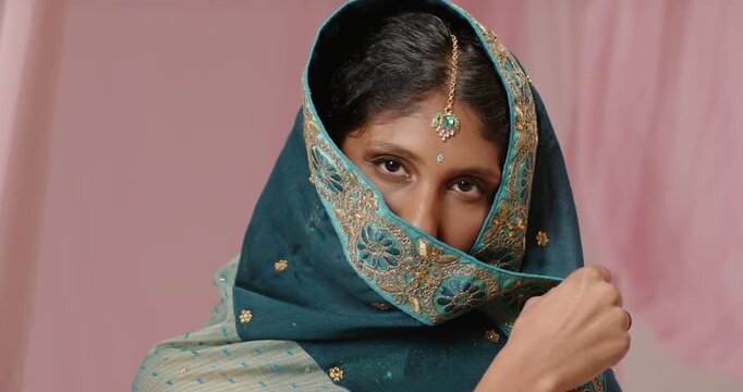 Adult Indian woman using right hand, pulling dupatta down and revealing maang tikka for portrait