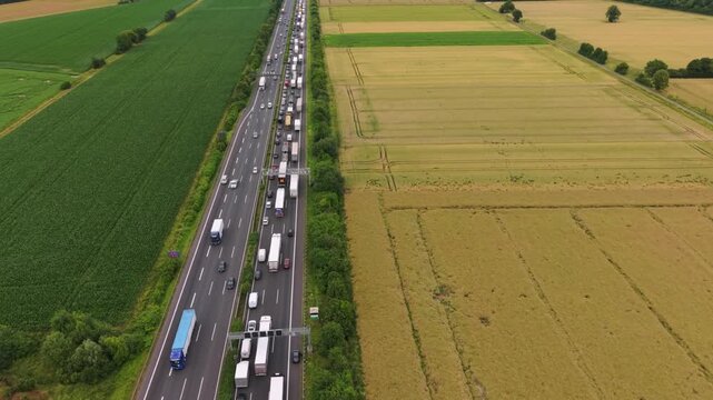 Aerial perspective of a congested highway with vehicles traveling alongside lush green fields and golden agricultural land, illustrating transportation dynamics