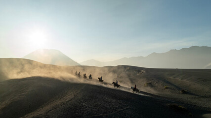 Tenggerese horse riders crossing the volcanic landscape around Mount Bromo in East Java, Indonesia, surrounded by drifting volcanic sand and dust. © huong