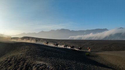 Tenggerese horse riders crossing the volcanic landscape around Mount Bromo in East Java, Indonesia, surrounded by drifting volcanic sand and dust. © huong