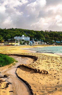 View across the sandy La Toc Beach towards a tropical resort surrounded by lush green hills in Saint Lucia.