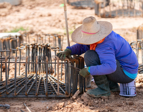 Construction worker tying steel rebar with wire using pliers for a concrete foundation cage at a building site.