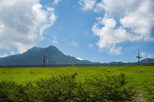 A long wooden fence stands along a grassy reservoir embankment beneath distant mountains and dramatic clouds in South Korea.