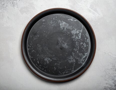 Round black ceramic serving platter with brown rim on light gray textured surface