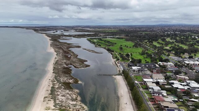 Aerial drone view over the Laverton Creek estuary and coastal wetlands at Altona, Melbourne, Victoria, Australia. Meandering tidal channels, sandy spits, saltmarsh, foreshore housing.