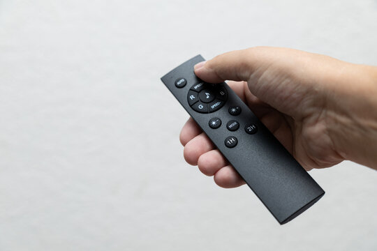 Hand holding RGB lighting remote control with color, speed, brightness, mode and timer buttons against clean neutral background.