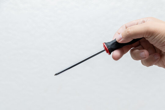 Hand holding Phillips screwdriver against clean white background, isolated tool with long metal shaft and black red handle.