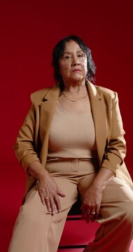 Vertical video: African American senior woman facing camera for portrait seated tilting in tan suit
