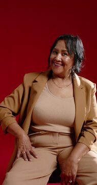 Vertical video: Senior African American woman smiling and laughing as camera zooming in red set
