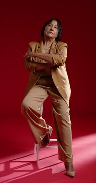 Vertical video: African American senior woman sitting on stool in studio posing and smiling