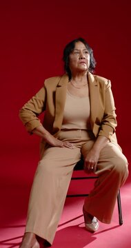 Vertical video: Senior African American woman shifting on chair in blazer after cue on red set