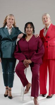 Vertical video: Female trio posing in studio for portrait, camera cueing hands on senior on stool
