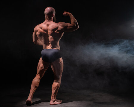 A male bodybuilder poses in shorts, showing off his back muscles.
