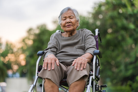senior woman suffering from knee pain while sitting in wheelchair at park