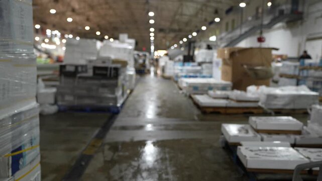 Stock footage of a worker walking through a busy industrial warehouse filled with packaged goods and logistics materials, representing supply chain operations.
