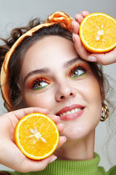 Portrait of a young woman with halves of oranges in her hands. Female with bright make-up on face.