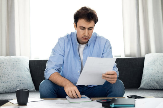 Worried man reading unpaid utility bills. Rising energy prices, household expenses, and inflation cause financial problems and economic crisis due to high cost of living.