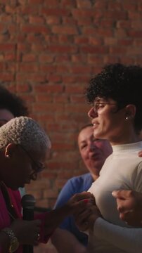Diverse congregation praying together and laying hands on young woman holding hands inside church against brick wall for spiritual intercession healing and faithful support
