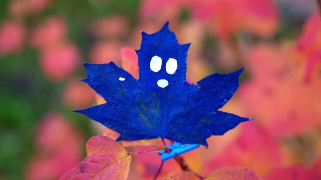 Autumn leaves decorated with dark black ghost faces hanging among colorful tree branches in seasonal woodland setting. Painted foliage with expressive spooky characters creates playful Halloween