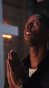 African American man holding hands together in prayer with head tilted upward during church worship service indoors for spiritual grace and faith
