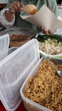 Close-up video of a food vendor's hands carefully wrapping nasi pecel, a traditional Indonesian rice dish served with mixed vegetables and savory peanut sauce, for a customer. Authentic local street f