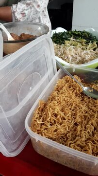 Close-up video of a food vendor's hands carefully wrapping nasi pecel, a traditional Indonesian rice dish served with mixed vegetables and savory peanut sauce, for a customer. Authentic local street f