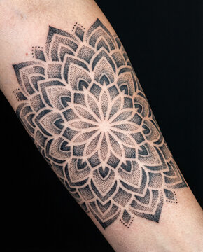 Geometric dotwork mandala tattoo with symmetrical lotus petals on human forearm