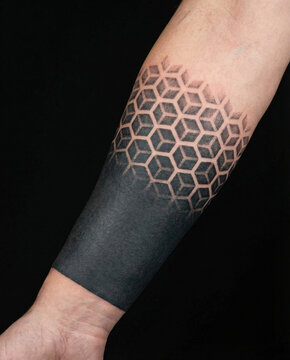 Geometric 3D isometric cube pattern fading into a solid blackout cuff tattoo on a lower forearm